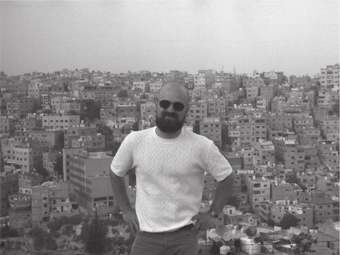 Portrait of a person standing in front of a dense hillside cityscape. Black and white.