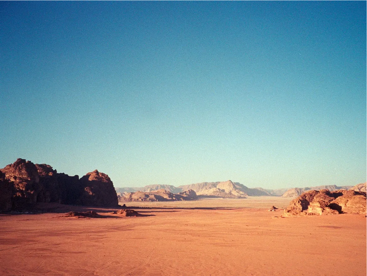 A wide desert valley flanked by rock formations under a clear blue sky.
