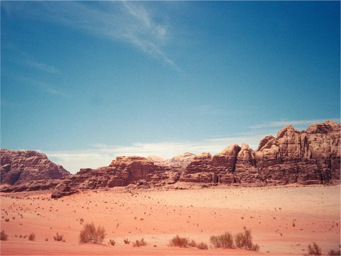 Layered rock formations rising above a desert plain scattered with scrub brush.