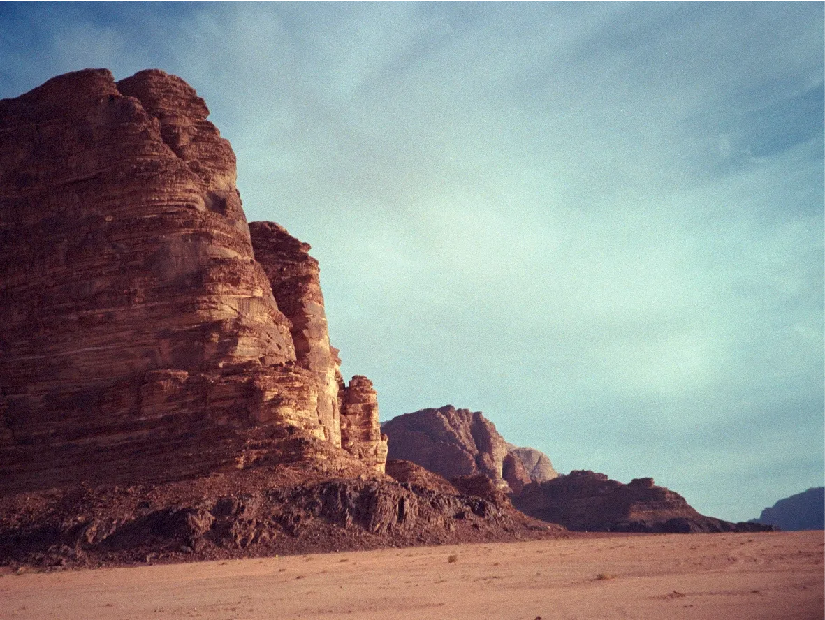 A tall sunlit rock formation against a hazy sky, with a desert plain below.