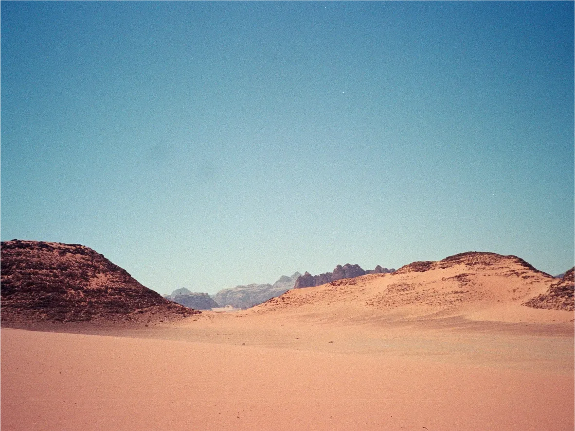 Sand dunes framing a distant mountain range in the desert.