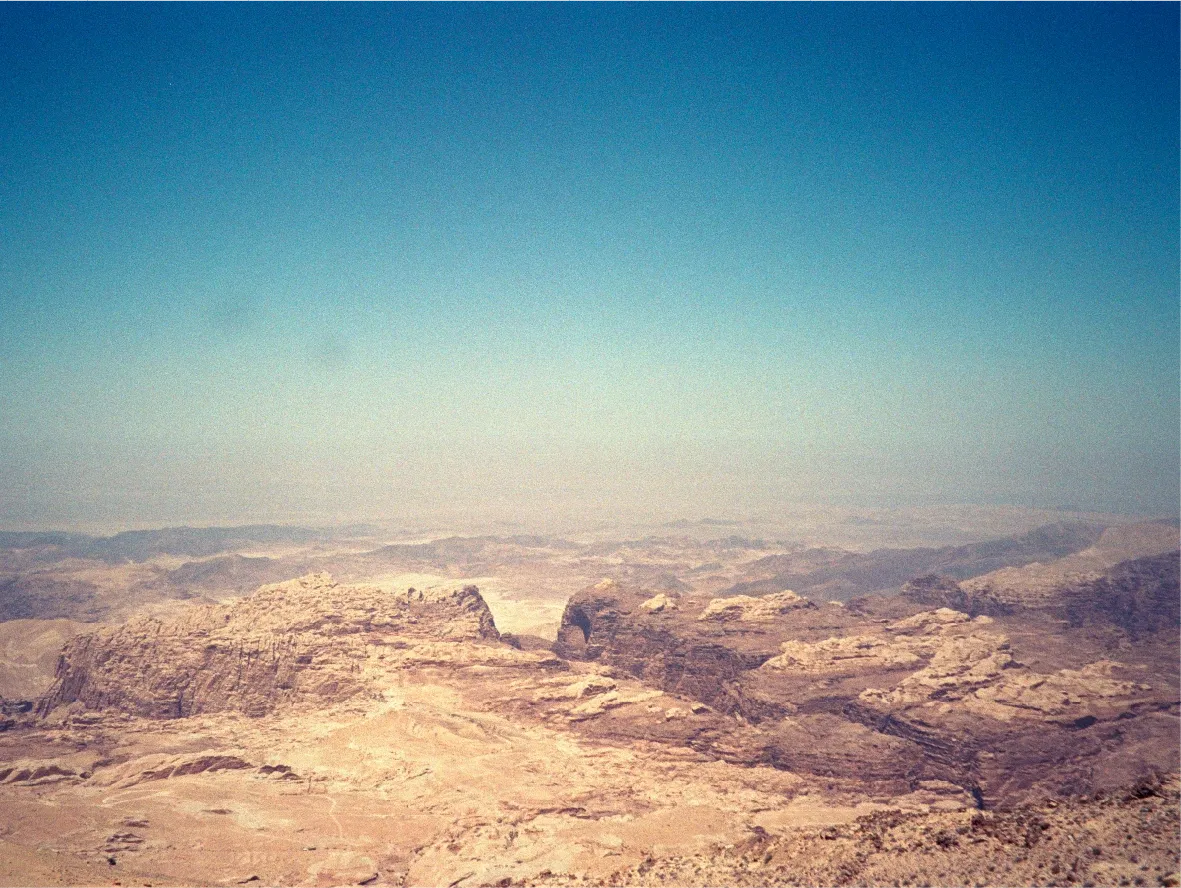 An aerial view of a vast canyon and mountain range under a hazy sky.